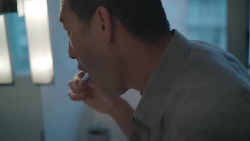 Young man looking in the mirror brushes his teeth in the bathroom at home