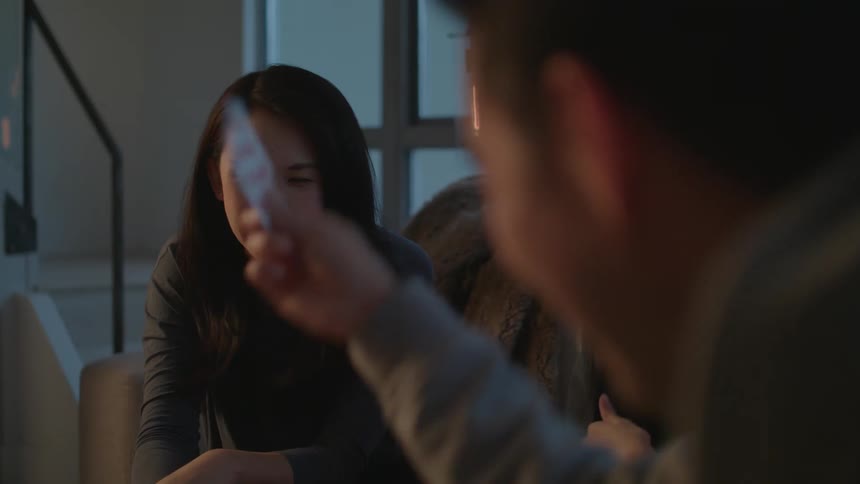A family sits on a couch in a living room laughing as they play a card game