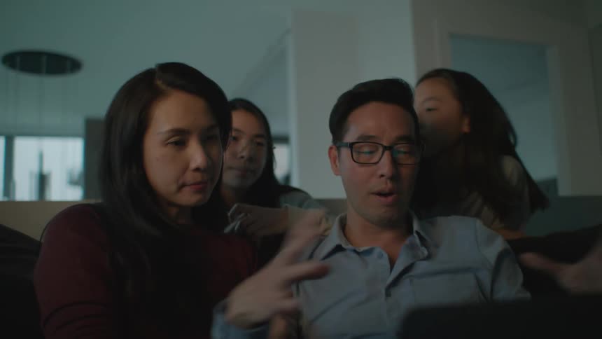 A group of people are gathered around together on a couch looking at a laptop