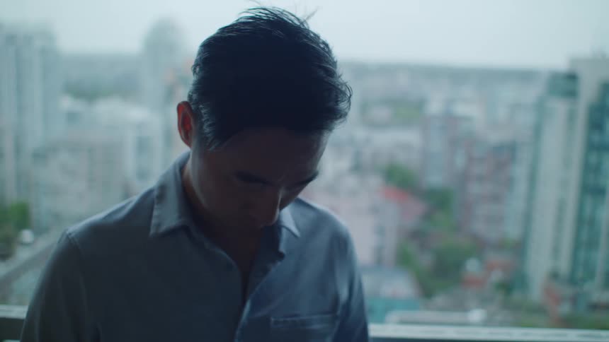 A man has his head down as he stands in front of a window