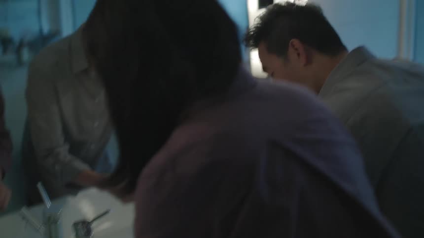 A man brushes his teeth and his wife comes up and kisses him on the cheek and then begins brushing her teeth