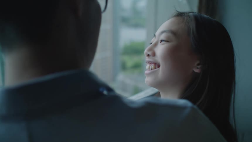 Father and daughter talk and smile while looking out the window at home
