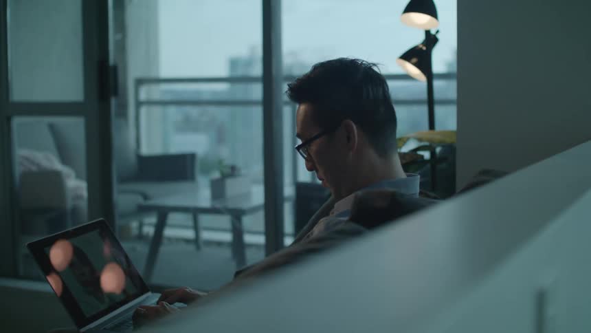 A man sits at home with his laptop and types and video chats with someone
