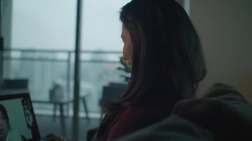 A woman is smiling at a laptop as she sits on a couch