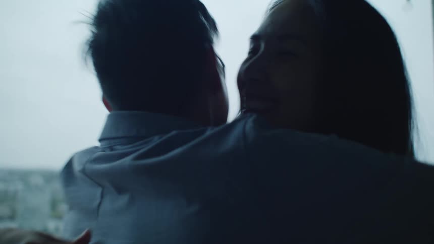 Couple stands on balcony pointing out sites of city to each other before smiling and hugging each other