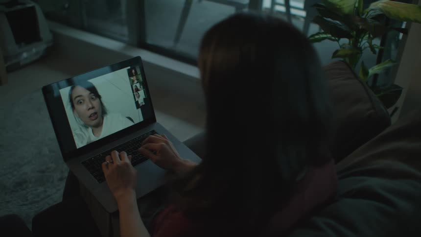 Woman talking to a friend on a video call on a laptop while sitting on a couch at home