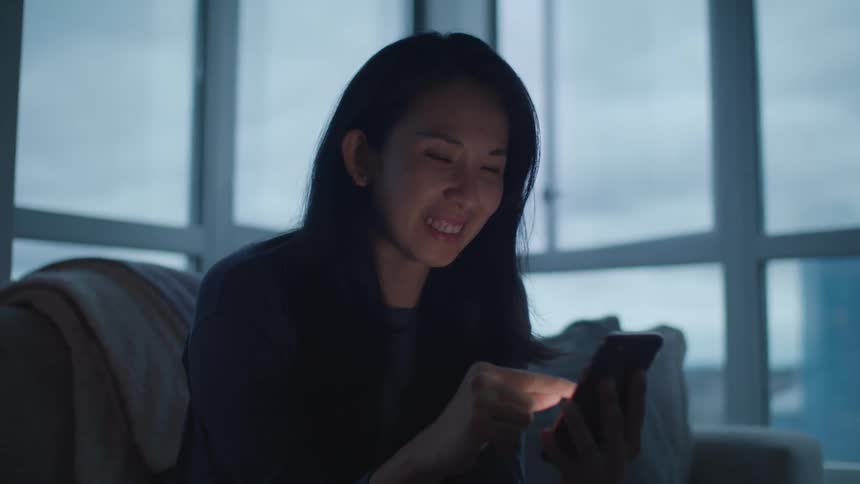 Woman sitting on the couch at home smiles while using a smartphone