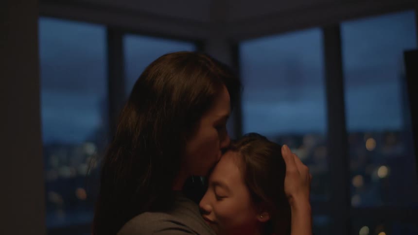 Mother hugs and kisses daughter on the living room of an apartment in the city