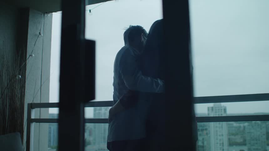 An asian couple are on a balcony hugging and smiling