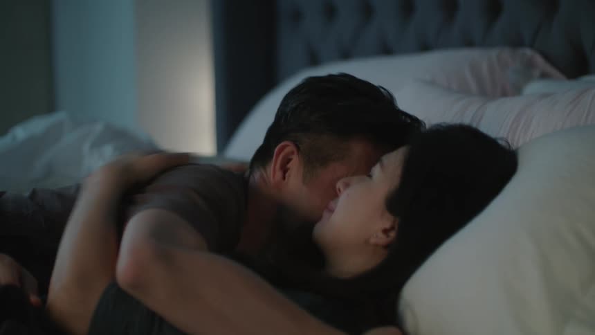 A man and woman hug and kiss as they lay in a bed