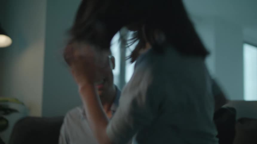 A man and a girl sitting on a couch in a room looking at a laptop with a wall and window in the background