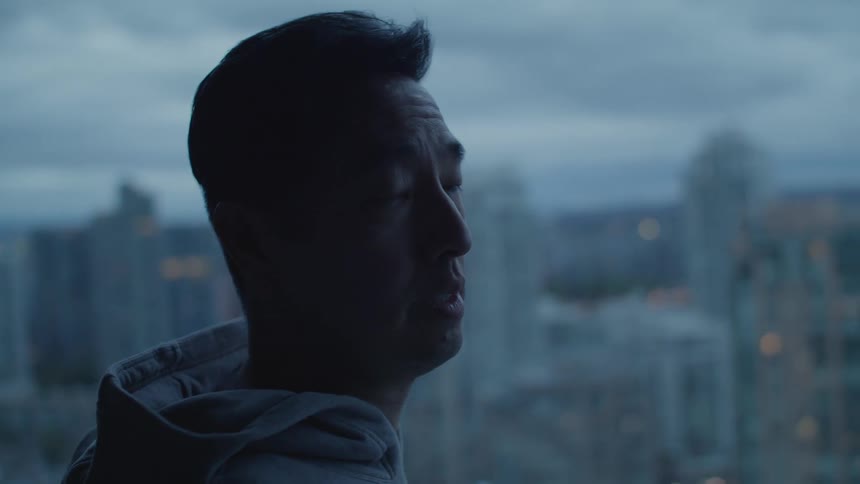 A man stands at a window and looks out at the city skyline