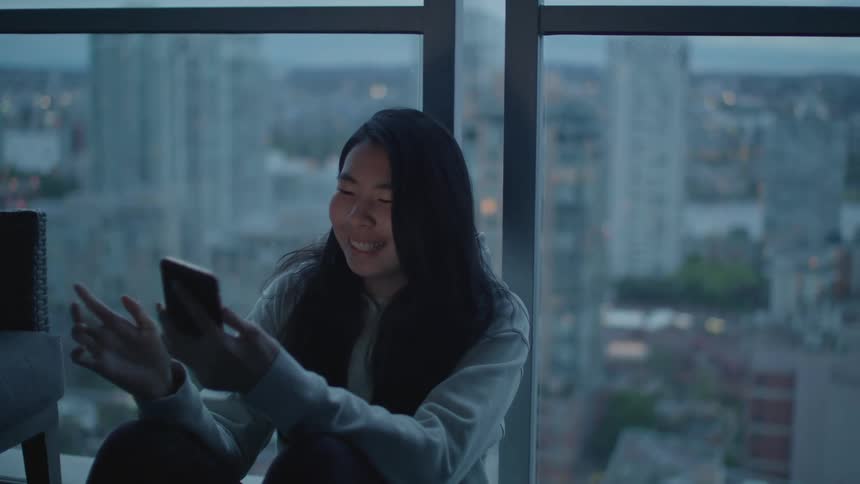 Young woman sitting near a window on an apartmet picks up her smartphone