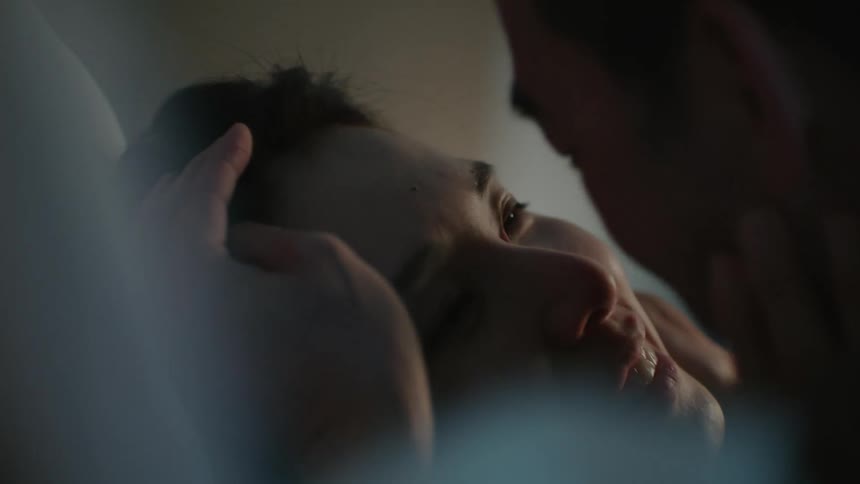 A man and a woman in a room on a bed kissing with a wall in the background