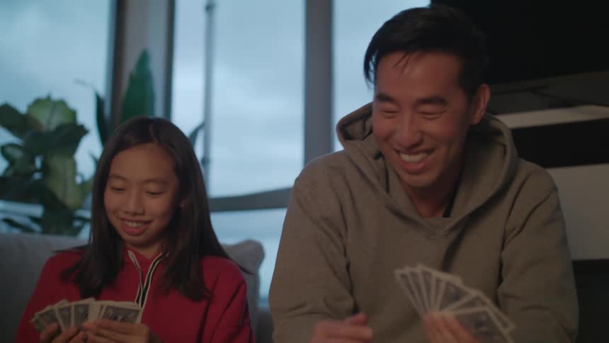 A man a woman and two girls in a room playing cards on a table with a wall and window in the background
