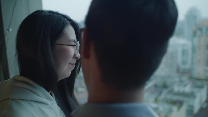An asian couple laughing and smiling in a room overlooking a city