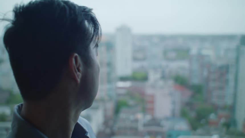 A sad looking man turns to look out the window at the city