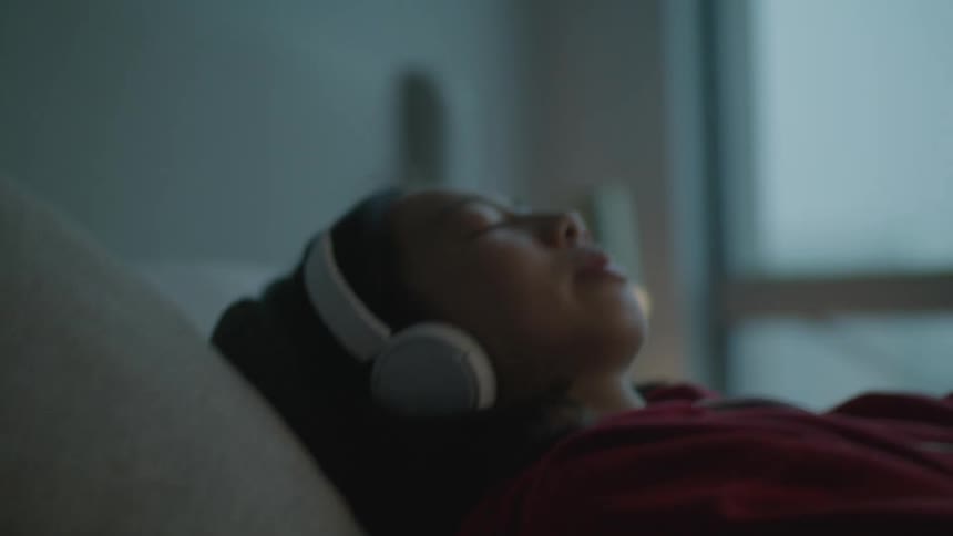 A woman has her eyes closed as she lays back onto a pillow on a bed
