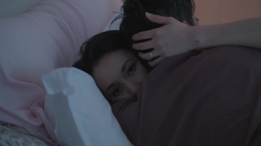 A couple embraces as they lay in their bed at home