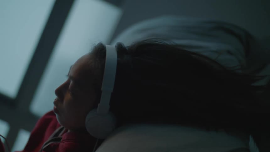 A young girl with headphones on uses her cellphone at home