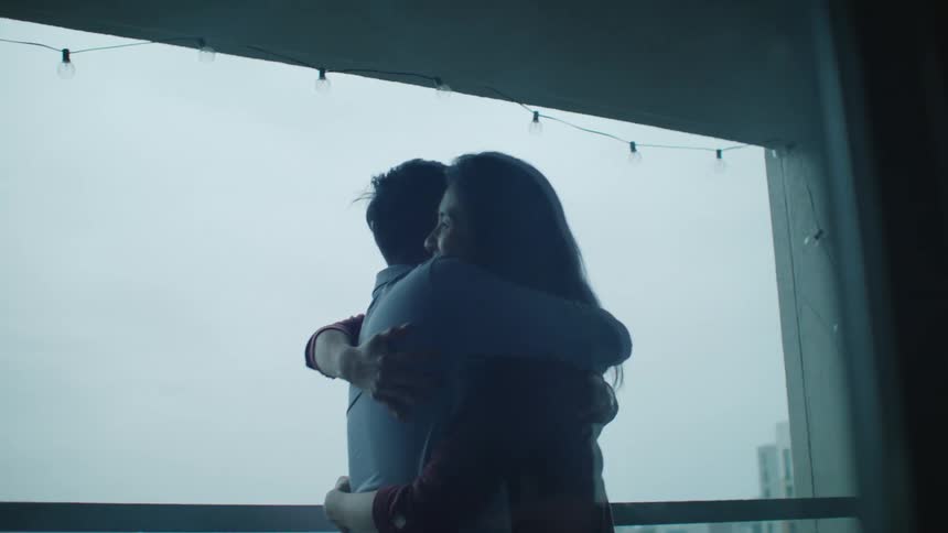 Young couple standing next to a window in an apartment hug each other