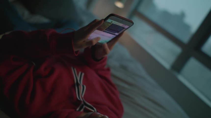 A woman is laying in bed texting on her cell phone