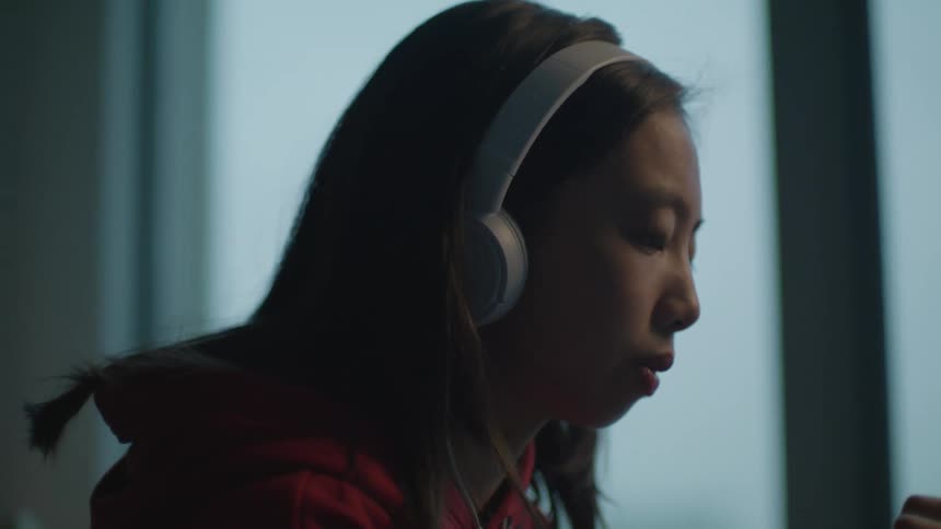 Teenager wearing headphones listens to music in her bedroom