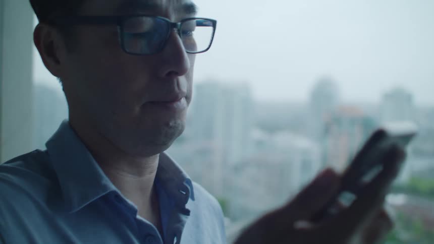A man stands by a window talking on a video call on his phone