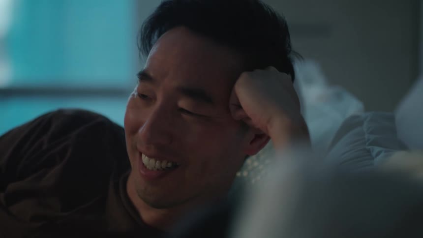 Man laying in bed smiling and talking to his partner