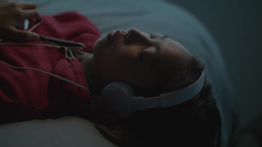 Girl wearing headphones listening to music laying in bed at home