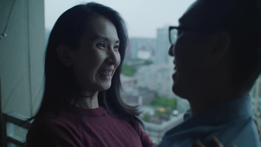 A man and woman at home hug and kiss and laugh on a balcony