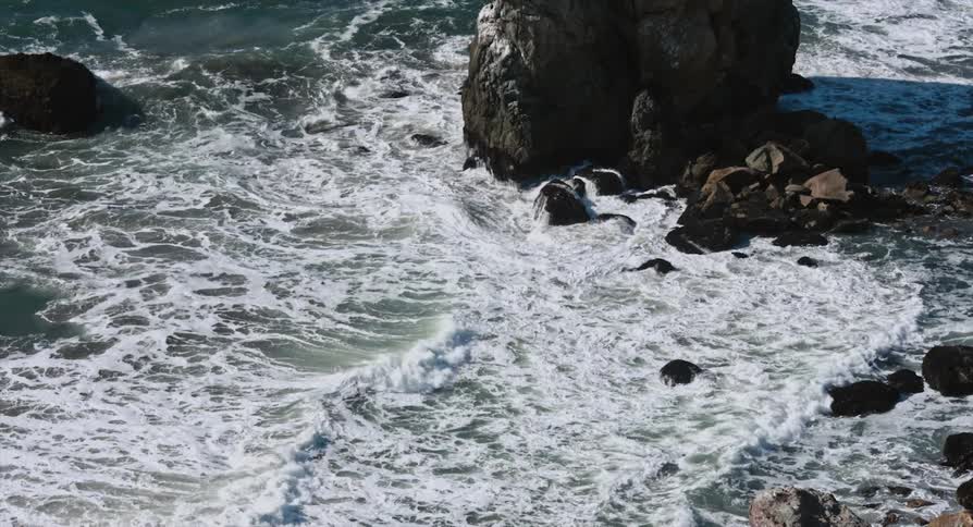 Seabird flies over ocean waves near rock outcropping