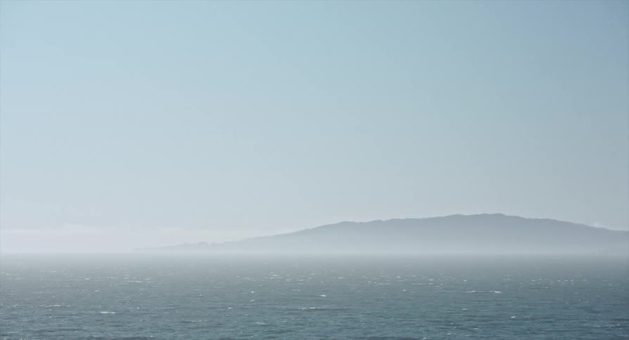 Rough water and waves under a foggy sky with a mountain in the distance