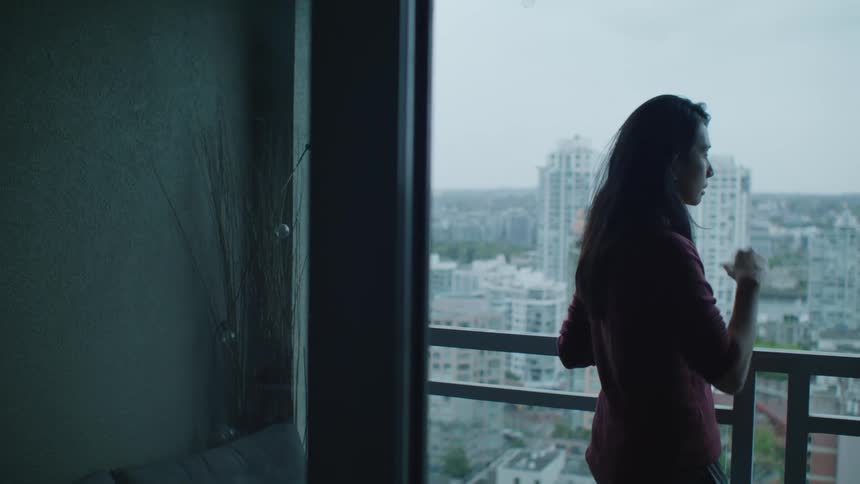 A woman stands on her balcony and looks in to her home and then towards the skyline in front of her