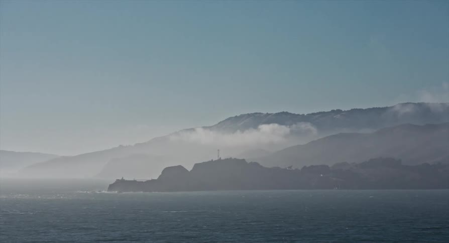 Rough water and waves under a foggy sky and a mountain along the coast