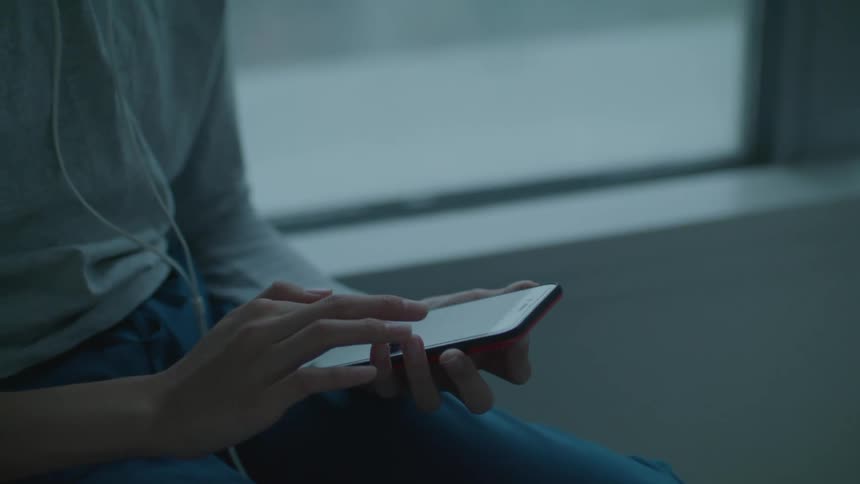 A young woman listens to music from her smartphone using headphones while sitting indoors during the day