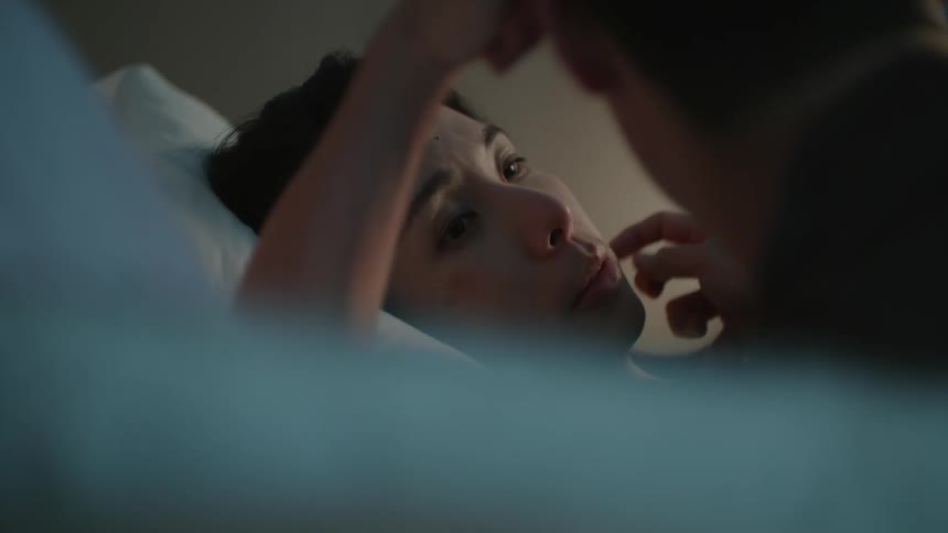 A female is laying down looking upset as a man strokes her face