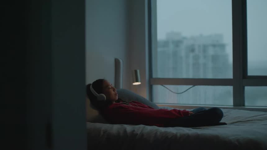 Girl wearing headphones listening to music on the bed at home
