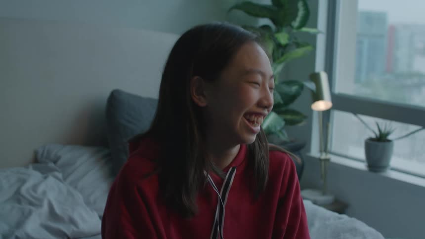 Two women sit on bed near window laughing together