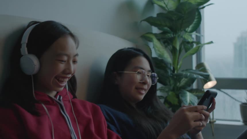 Two girls sit down to listen to music on a cellphone