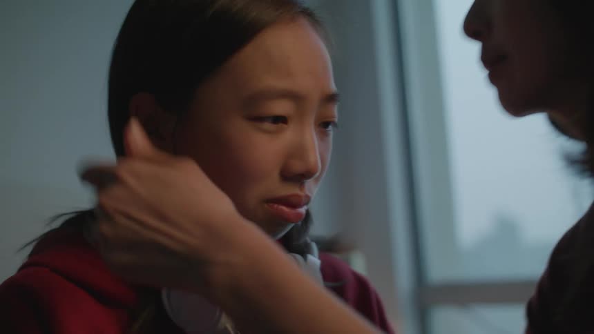 A boy with headphones in a room being hugged and kissed by woman with a wall in the background