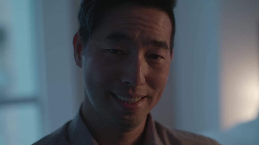 A man in a room smiling and staring with a wall and window in the background