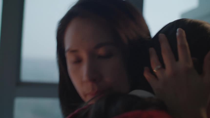 A young girl with headphone on looks down at the ground and then her mother walks in takes the headphones off and kisses and hugs and consoles the girl who sobs in her mothers arms