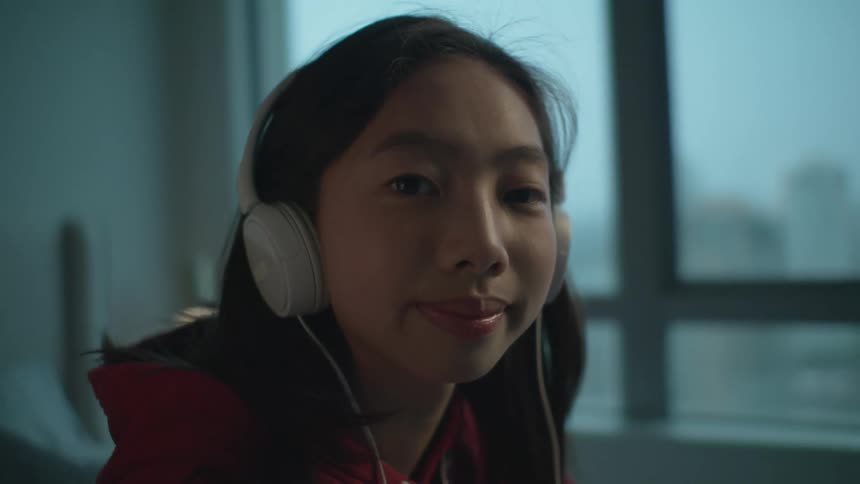 A teenage girl wearing headphones stares into the camera and smiles