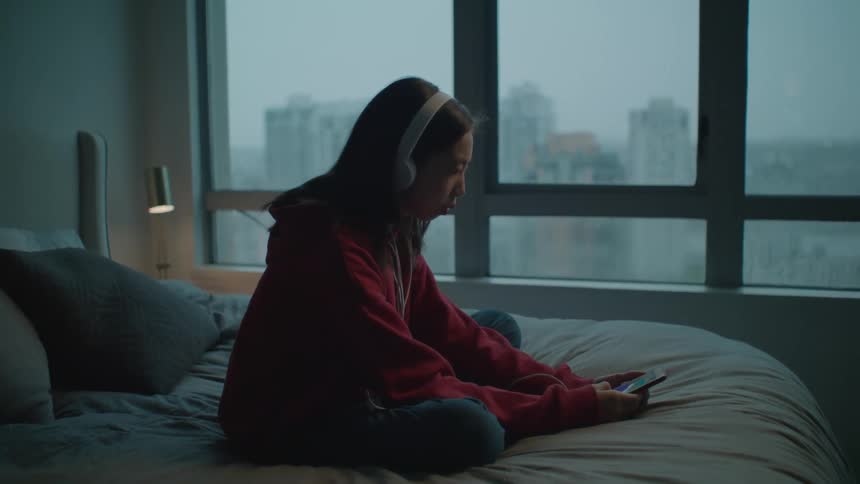 A woman is sitting on a bed listening to music and nodding her head