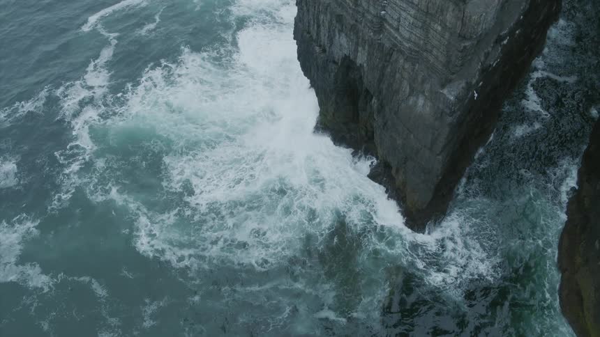 Waves crashing into a cliff as birds fly above