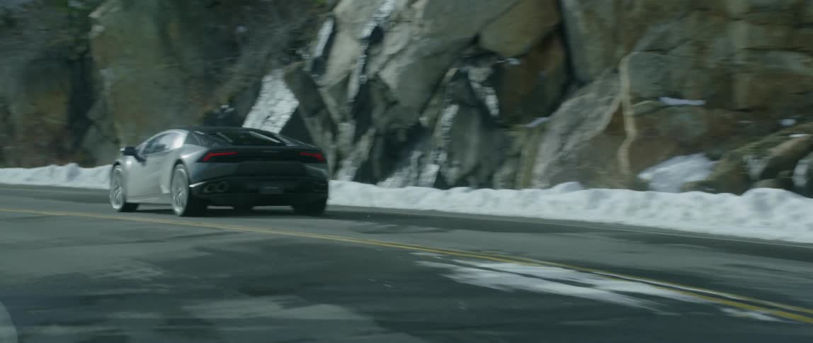 A black lamborghini travels down a snow covered road on a winter day