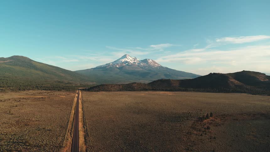A desert landscape with a road with a vehicle with a mountain range the sky and clouds in the background