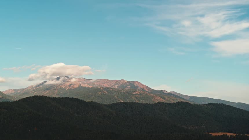 Tree covered mountains sit below taller snow capped mountains