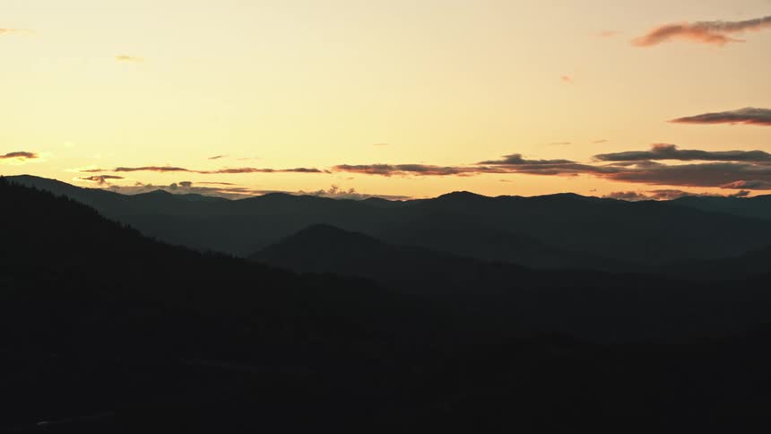 Red tinted and dark clouds sit in red sky over dark misty silhouetted mountains and hills